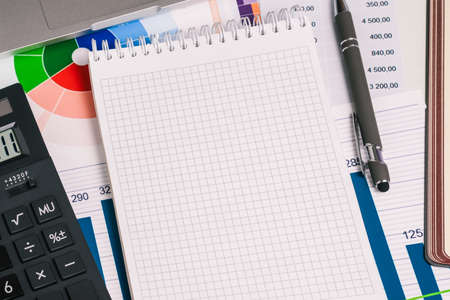 Empty Notepad page, a calculator, a pen, and financial papers with numbers on the desktop. Trade, investment, and banking.の写真素材