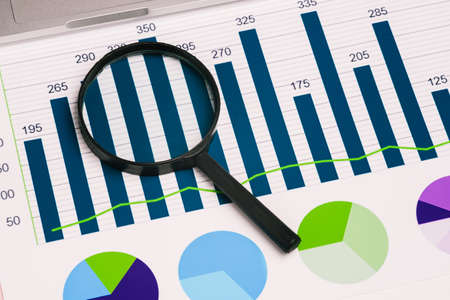 Glass magnifier and diagrams on the desktop. Business concept and data analysis. A top view of a...