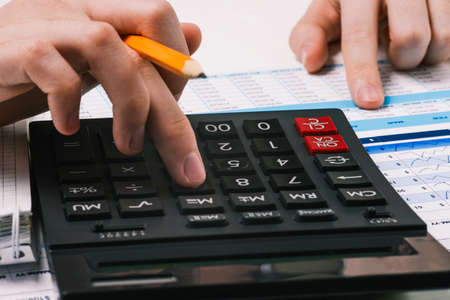Calculator and hands with a pencil. Desktop with financial and accounting documents. Person counts on a calculator and analyzes the data.の写真素材