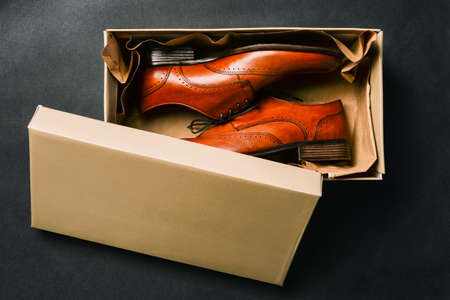 Men shoes in an open box, isolated on a black background. Open Shoe box. New shoes from the store. Brown shoes made of genuine leather. The view from the topの写真素材
