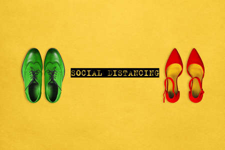 Multi-colored mens and womens shoes on a yellow background with the text Social distancing. The concept of prevention of the risk of infection and coronavirus diseaseの写真素材