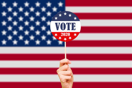 Hand and button for voting in elections on the background of the American flag. The 2020 US...