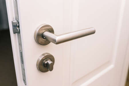 Open the white door. Modern chrome handle in your hotel room or home. Entrance to an apartment, office, or bedroom. Door detail. Interior of a house or hotel.の写真素材
