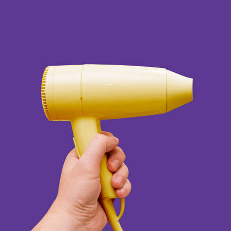 Yellow background on purple background. A man holds a dryer in his hand. A tool for a beauty salon...