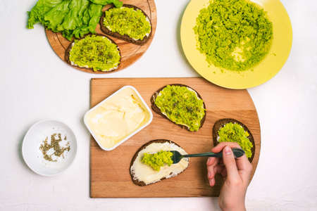 Female chef prepares an avocado sandwich. Table with a plate of mashed avocado, spices, bread and a pack of cream cheeseの写真素材