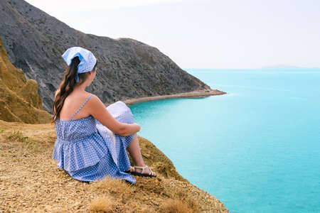 Young girl on the mountain. The traveler looks at the rocks and the ocean. Seascape. Hiking, adventure and active tourismの写真素材