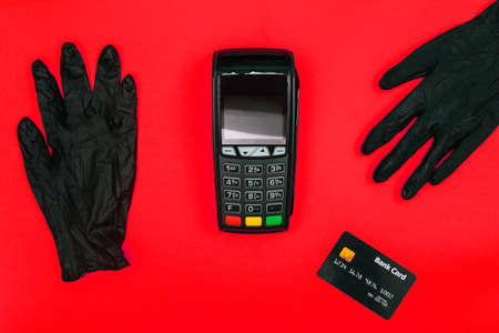 Payment terminal, disposable gloves and a bank card for paying for goods on a red background. Safety due to coronavirus infection. Precautions and protection in stores. Business and technologyの写真素材