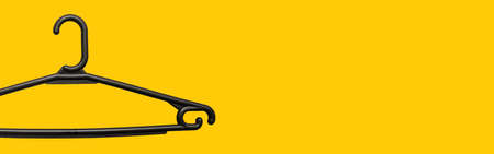 Plastic black hanger on a yellow background with copy space. Holder for household and business belongings. The concept of selling goods in an online storeの写真素材