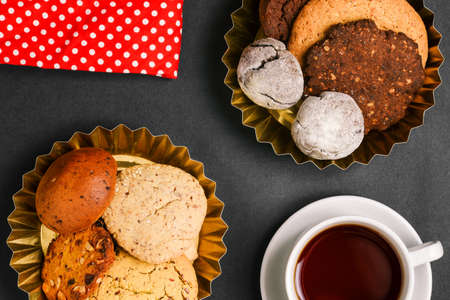 Composition of a tea cup, sweet homemade cakes, cookies and red polka dot fabric on a dark background. Cooking concept. Top view, close-up. Food background, culinary recipesの写真素材