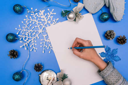 The girl writes on a white sheet of paper. Christmas greeting card. Composition of New Years toys, garlands, snowflakes and cones. Winter, Christmas backgroundの写真素材