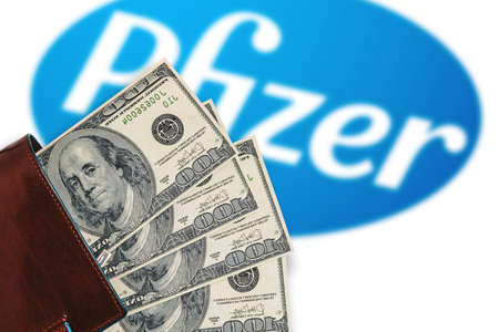 Wallet with dollars and a blurry Pfizer logo. Pfizer vaccine cost concept against coronavirus,...