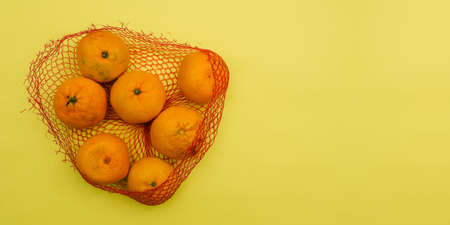 Tangerines in an open package isolated on a yellow background with copy space. Fresh fruits. Vegetarian food. Healthy and wholesome foodの写真素材