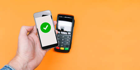Transaction approval process. Contactless payment for purchases with a mobile phone. Payment terminal and hand with a gadget. Top view, flat lay. Copy spaceの写真素材