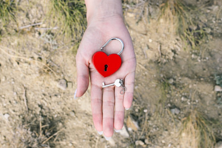 Lock and key in hand. Red metal lock in the form of a heart. Lock of love and key in the shape of a...
