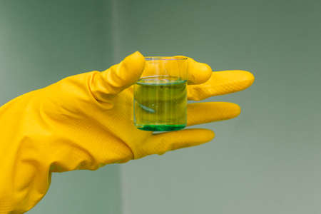 Hands in rubber yellow gloves hold a test tube with a green liquid. New drug development, chemistry experiment. Medical laboratoryの写真素材