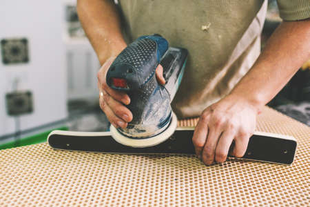 Carpentry workshop. Mans work process. Processing a wooden part with a grinding machine. Manufacturing of furniture from wood and plywood.の写真素材
