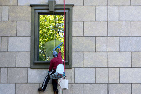 A man hanging on a rope and washing a windowのeditorial素材
