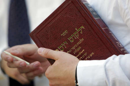 A jewish prayer holds holy book and wooden pencil in his hands 