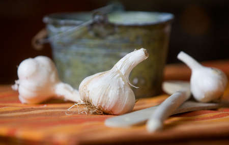 Wooden utensils and few heads of garlic in front of small metal bucket lying on a table cloth