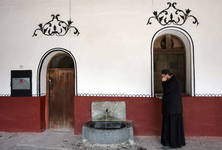 Orthodox priest use his cell phone near old fountain in Rila Monastery, Bulgaria のeditorial素材