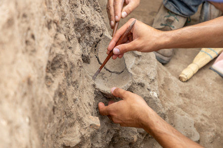 Team of researchers and students using specialized tools like trowels and hand brooms to clear soil from a trench at the ancient archaeological site.