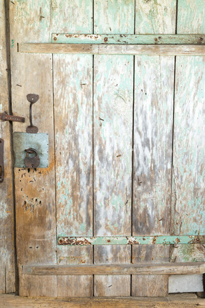 Wooden door with metal hinges with pieces of old green paint.の写真素材