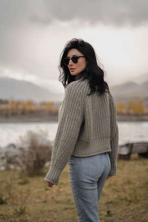 Brunette european girl stands with her back against the background of river and mountains. Autumnの写真素材