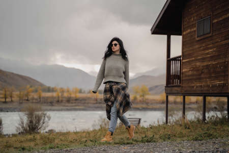 Brunette european girl walk with her back against the background of river and mountains. Autumnの写真素材