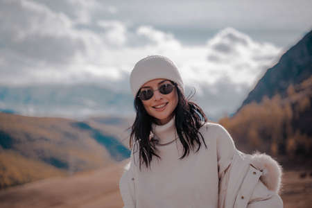 Beautiful stylish girl tourist posing against the backdrop of white snow peaks. Sunny. Close upの写真素材