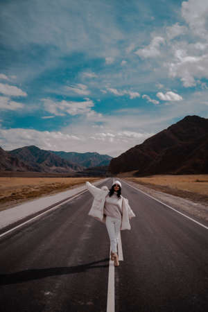 Beautiful stylish girl travel blogger is walking along solid line of road. Happy. Sunny. Verticalの写真素材