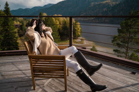 Beautiful girl in stylish light clothes and brown hat sits on roof in rays of sun and chillの写真素材