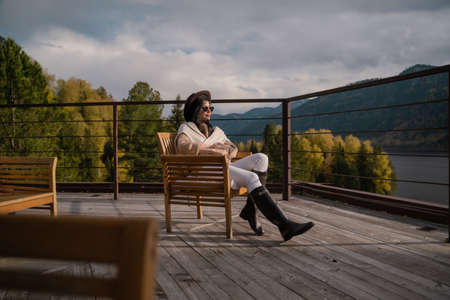 Beautiful girl in stylish light clothes and a brown hat sits on the roofの写真素材