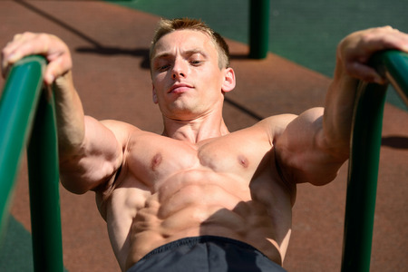 Fitness strength training workout bodybuilding concept background - muscular bodybuilder handsome man doing exercises in outdoor gym naked torsoの写真素材