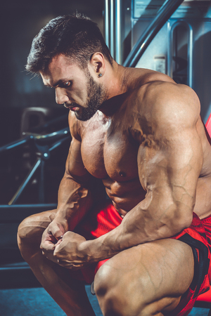 Handsome fit caucasian muscular man flexing his muscles in gym on diet. Brutal bodybuilder powerful training and execute exerciseの写真素材