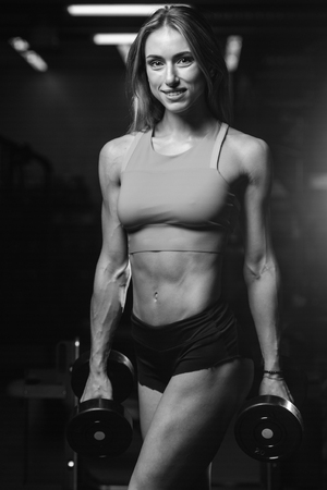 Caucasian pretty fitness girl on diet training pumping up muscles with dumbbell and barbell in gymの写真素材