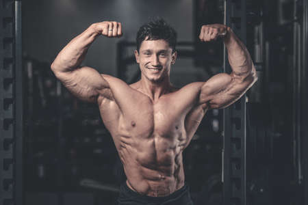 Handsome power athletic man on diet training pumping up muscles with dumbbell and barbell. Strong...