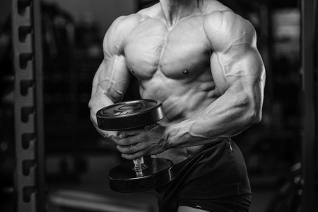 Handsome power athletic man on diet training pumping up muscles with dumbbell and barbell. Strong bodybuilder with six pack, perfect abs, shoulders, biceps, triceps and chestの写真素材