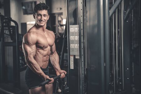 Handsome power athletic man on diet training pumping up muscles with dumbbell and barbell. Strong bodybuilder with six pack, perfect abs, shoulders, biceps, triceps and chestの写真素材