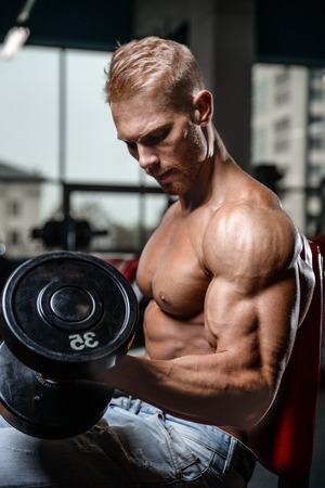 Handsome power athletic man on diet training pumping up muscles with dumbbell and barbell. Strong bodybuilder with six pack, perfect abs, shoulders, biceps, triceps and chestの写真素材