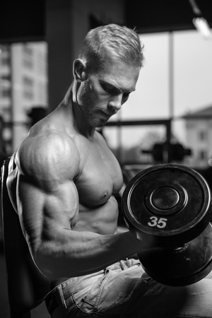 Handsome power athletic man on diet training pumping up muscles with dumbbell and barbell. Strong bodybuilder with six pack, perfect abs, shoulders, biceps, triceps and chestの写真素材