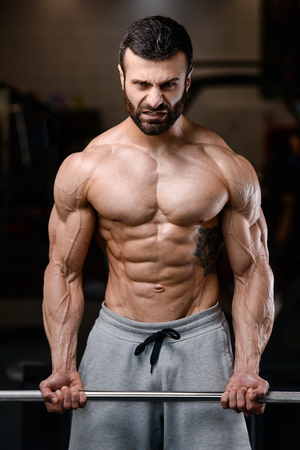 Handsome power athletic man on diet training pumping up muscles with dumbbell and barbell. Strong bodybuilder with six pack, perfect abs, shoulders, biceps, triceps and chestの写真素材