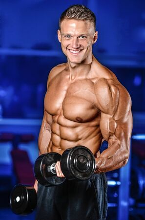 Handsome power athletic man on diet training pumping up muscles with dumbbell and barbell. Strong bodybuilder with six pack, perfect abs, shoulders, biceps, triceps and chestの写真素材