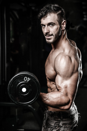 Handsome power athletic man on diet training pumping up muscles with dumbbell and barbell. Strong bodybuilder with six pack, perfect abs, shoulders, biceps, triceps and chestの写真素材
