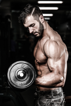 Handsome power athletic man on diet training pumping up muscles with dumbbell and barbell. Strong bodybuilder with six pack, perfect abs, shoulders, biceps, triceps and chestの写真素材