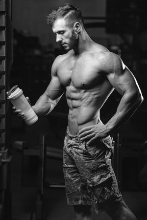 Muscular caucasian man on diet resting after exercise And drinking protein powder from shaker in the gymの写真素材
