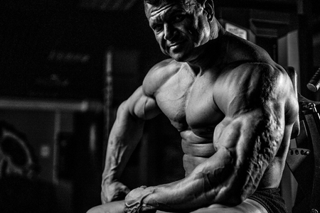 Brutal handsome Caucasian bodybuilder working out training in the gym gaining weight pumping up muscles and poses fitness and bodybuilding conceptの写真素材