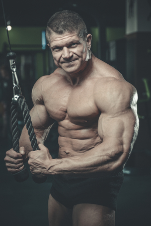Handsome muscular Caucasian man of model appearance working out training arms in gym gaining weight pumping up muscles bicep and tricep with dumbbells and on machines fitness and bodybuilding conceptの写真素材