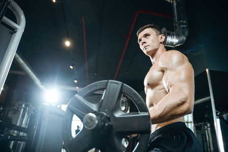 Handsome muscular Caucasian man of model appearance working out training arms in gym gaining weight pumping up muscles bicep and tricep with dumbbells and on machines fitness and bodybuilding conceptの写真素材