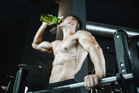 Beautiful sexy athletic young brunette Caucasian girl taking protein sports nutrition in the gym and posesの写真素材