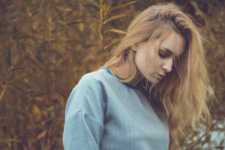 cute well dressed pretty young caucasian blonde hair adult teenage girl in fashion dress coat outdoor near farm house at mist countryside landscape field spring or autumn weather depressed moodの写真素材
